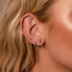 Close-up of a woman's ear adorned with the Amethyst Earring Trio Set, featuring pavé huggie hoops and purple gemstone earrings in multiple piercings.