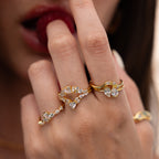 A hand adorned with gold rings, including the Diamond Curve Cluster Ring sparkling with diamonds, touches lips with a finger.