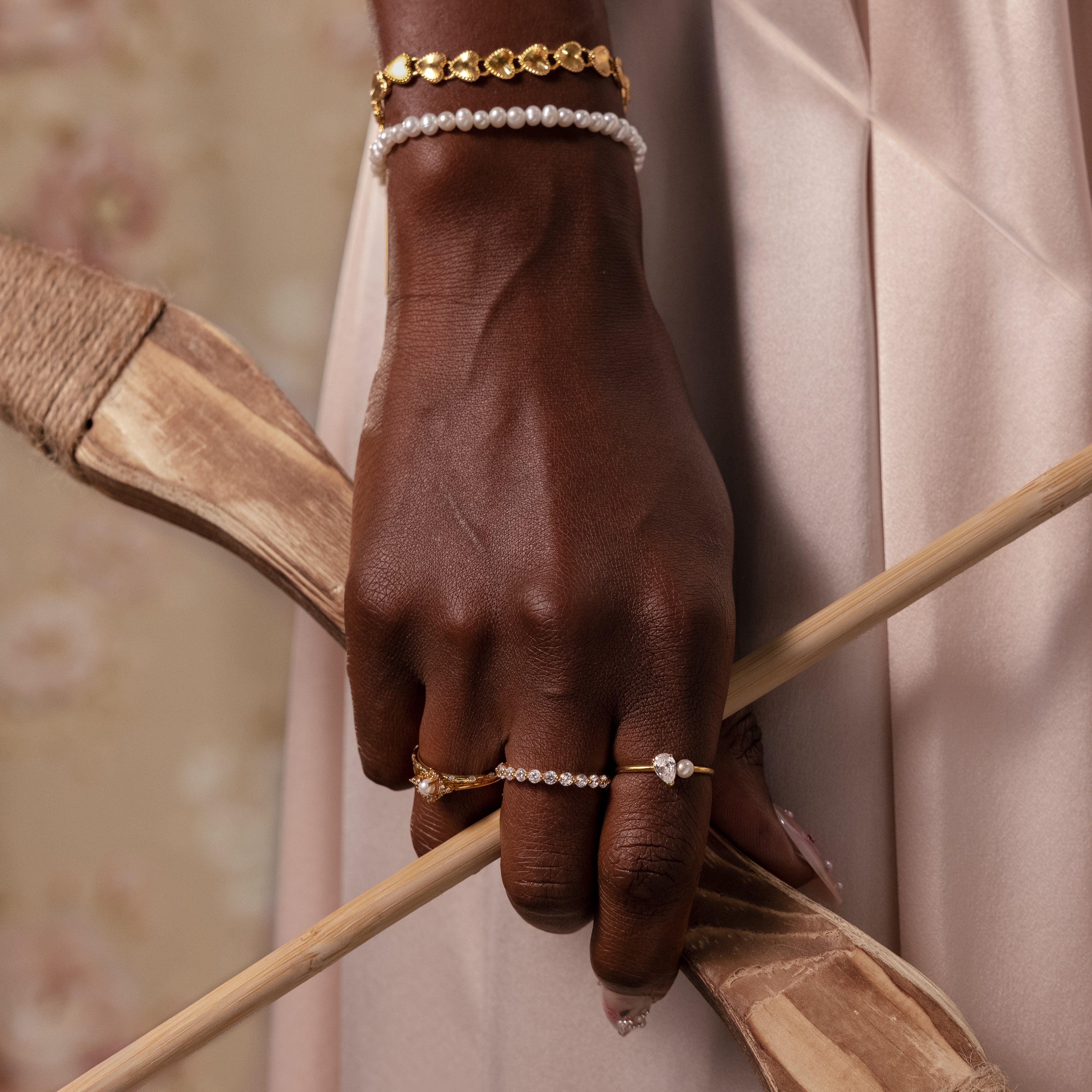A hand wearing the Vintage Pave Pearl Ring and gold jewelry holds a wooden bow against a soft beige background.