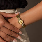 Someone wears the Diamond Mesh Timepiece, featuring a vintage look with a gold mesh band and diamond-accented round face, on their left wrist.