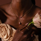 Woman in a floral dress holds a pink rose, wearing a gold Mixed Pink Tourmaline Capsule Necklace and a ring with pink stones.