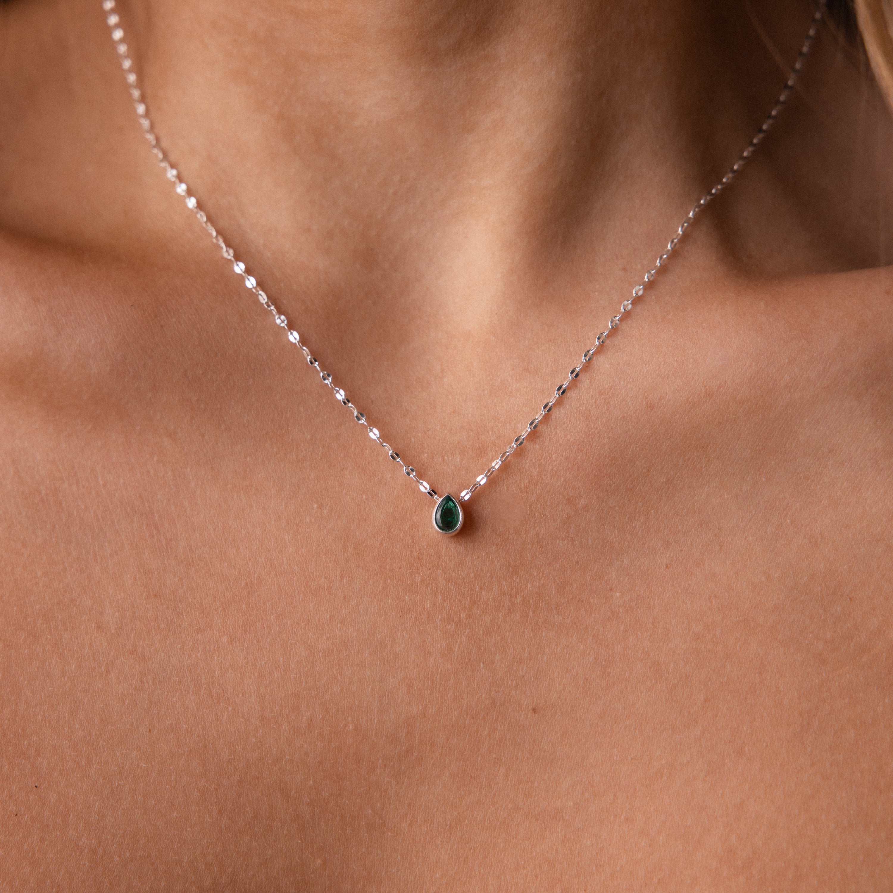 The Multiple Teardrop Birthstone Necklace in Sterling Silver features elegant green teardrop pendants that rest gracefully on a woman's neck, making it a beautiful piece of keepsake jewelry.
