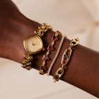 A wrist adorned with the Organic Mariner Chain Bracelet and gold watch, set against a soft beige background, highlights the allure of contemporary jewelry.