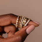 A hand with nude nails showcases the Art Deco Diamond Ring Set—five gold rings sparkling with diamonds—capturing vintage glamour against a neutral background.
