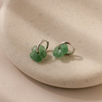 Jade Flower Hoops in Silver, featuring delicate jade flower charms, rest on a speckled beige ceramic dish—perfect for lovers of dainty earrings.