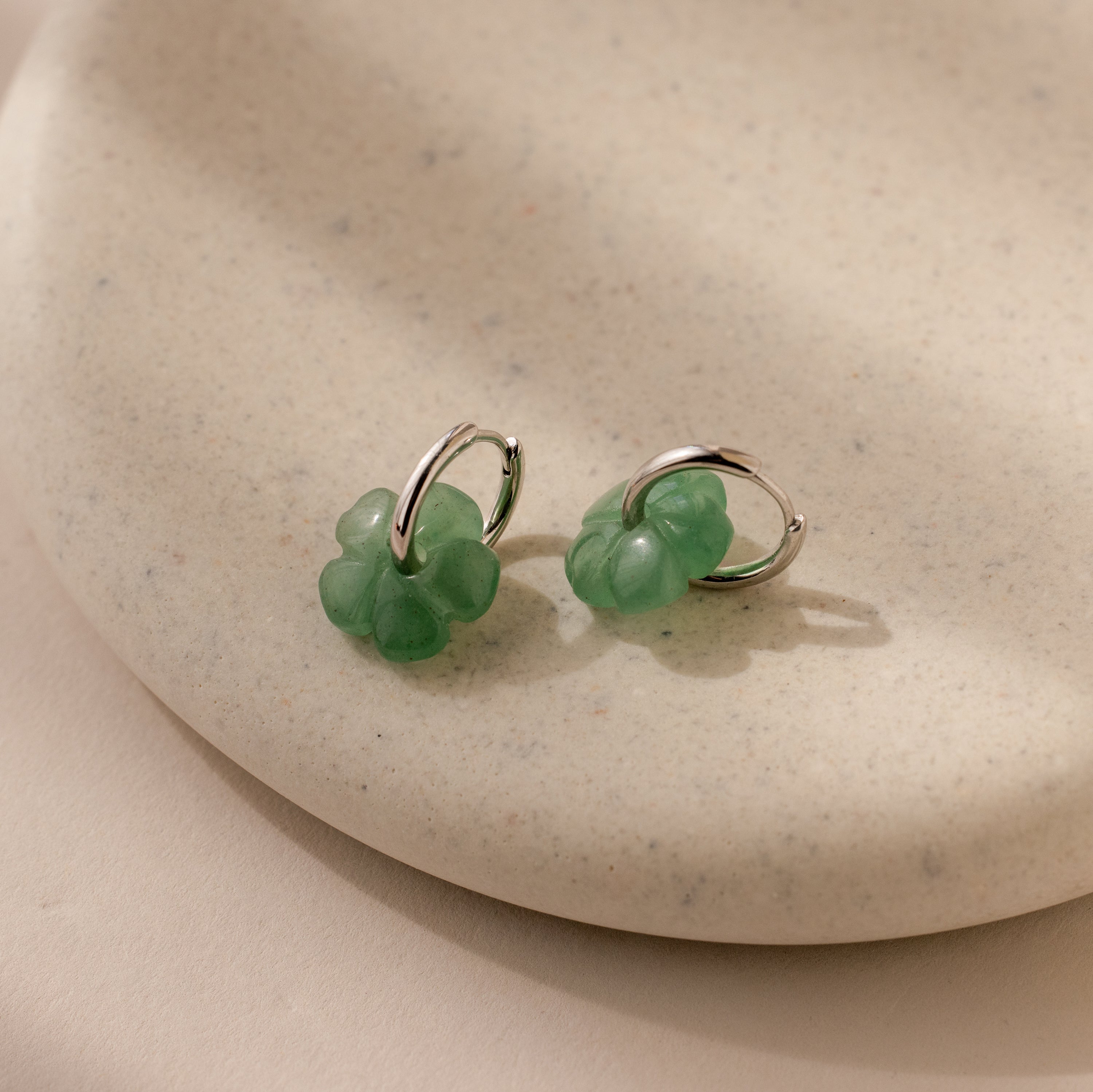 Jade Flower Hoops in Silver, featuring delicate jade flower charms, rest on a speckled beige ceramic dish—perfect for lovers of dainty earrings.
