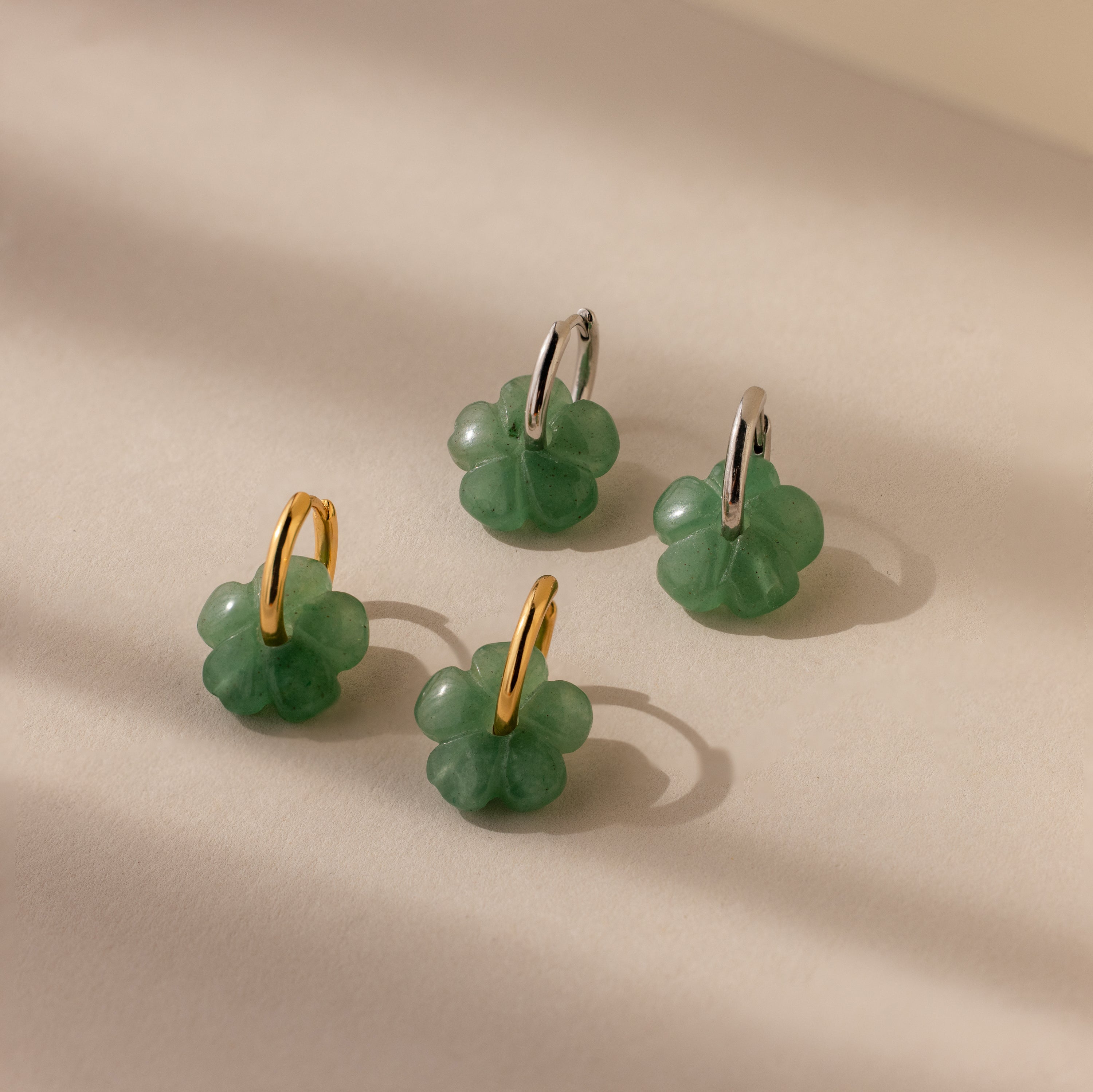 Four Jade Flower Hoops in Silver, clover-shaped charms with green jade-like detail, are arranged on a light beige surface.