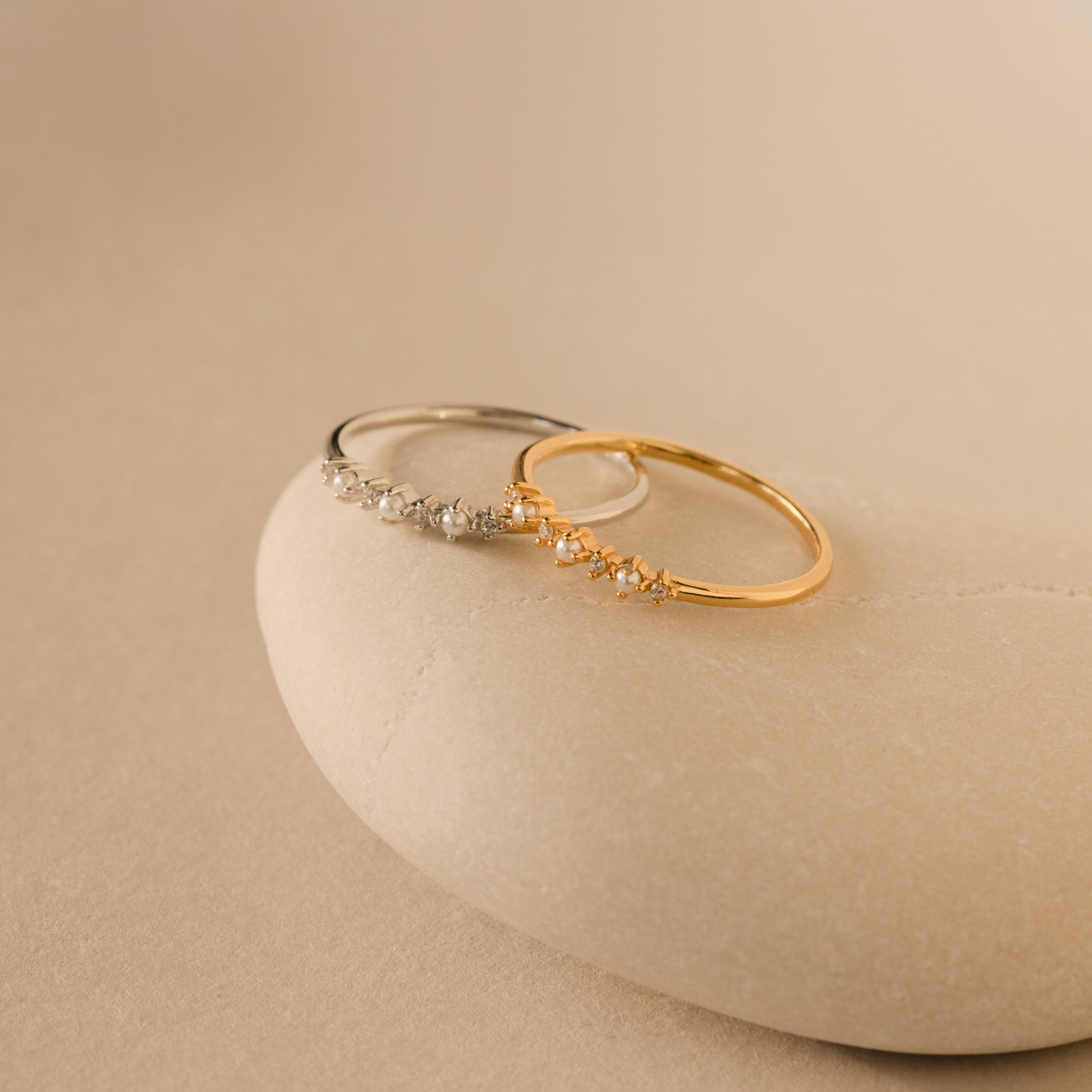 The Delicate Pearl Diamond Ring, crafted with elegant pearls and diamonds, shines on a smooth beige stone—ideal for stacking, layering, or as a unique engagement ring.