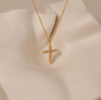 The Pave Cross Necklace in 18K Gold features a gold chain and a diamond-encrusted cross pendant, showcased on a soft cream-colored surface.