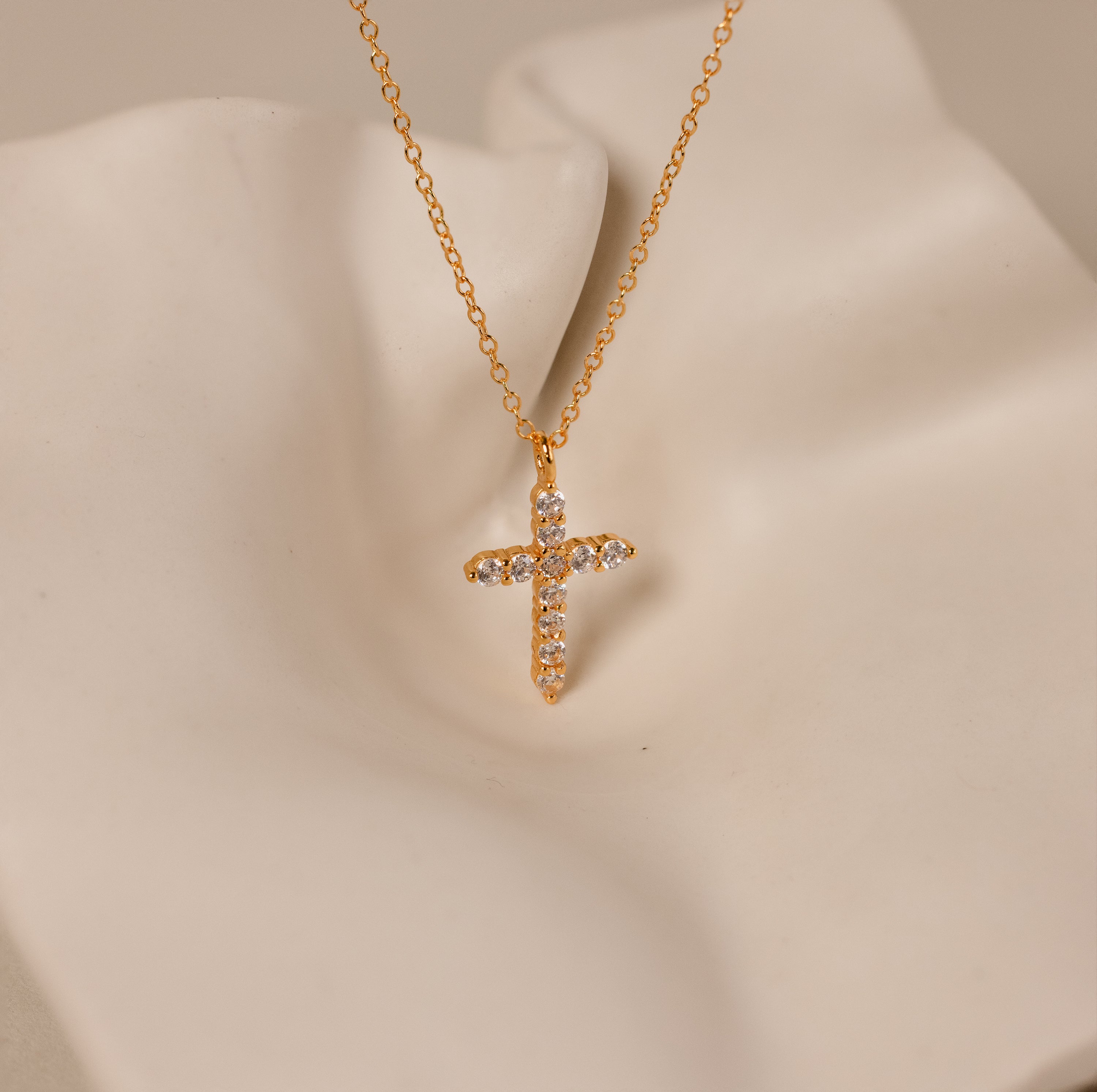The Pave Cross Necklace in 18K Gold features a gold chain and a diamond-encrusted cross pendant, showcased on a soft cream-colored surface.