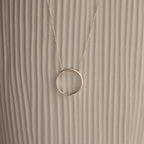 Inner Circle Necklace in Sterling Silver, featuring a simple circular pendant on a chain, shown against a textured beige background.