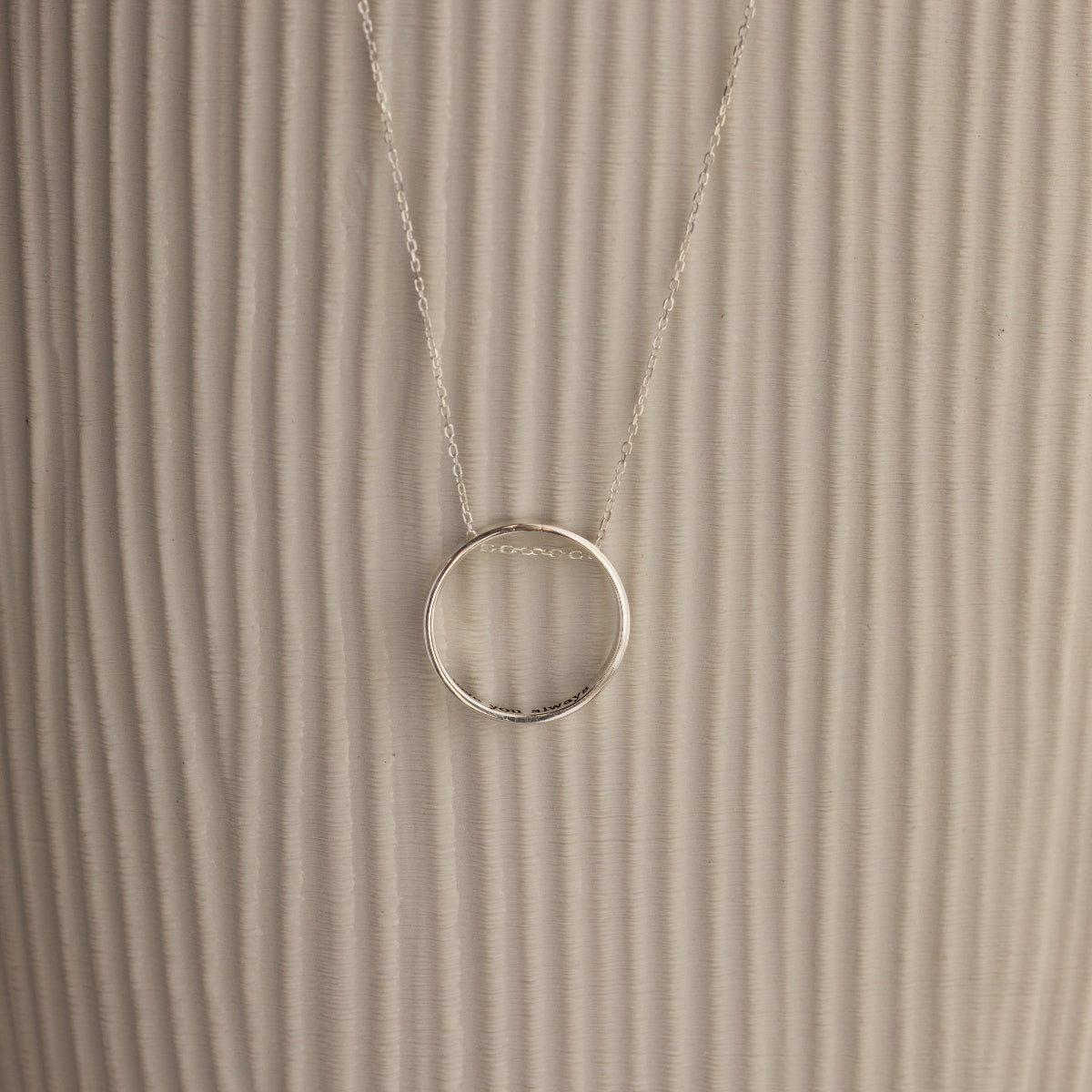 Inner Circle Necklace in Sterling Silver, featuring a simple circular pendant on a chain, shown against a textured beige background.