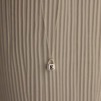 The Padlock Necklace features a silver chain with a small E-engraved pendant, offering a subtle and stylish fashion statement against a textured, light background.