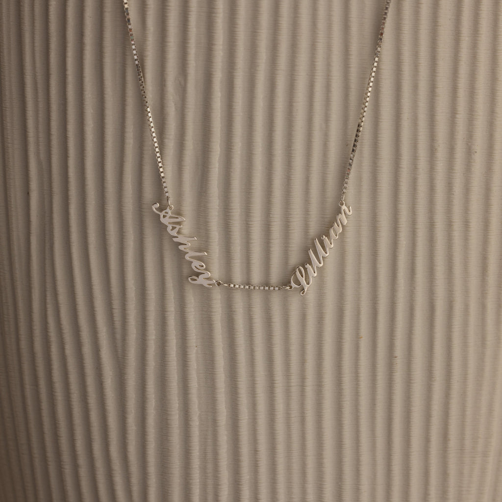 Necklace with 'Ashley' and 'Lillian' name charms in cursive on a textured brown background