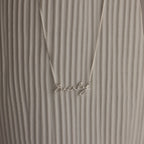 The Callie Box Chain Name Necklace features "Everly" in cursive on a delicate chain, shown against a textured, light background.