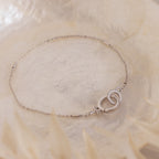 The Hinged Circle Charm Bracelet in Sterling Silver features two interlocking circles and is showcased on a soft, light-textured background for a delicate, minimal look.