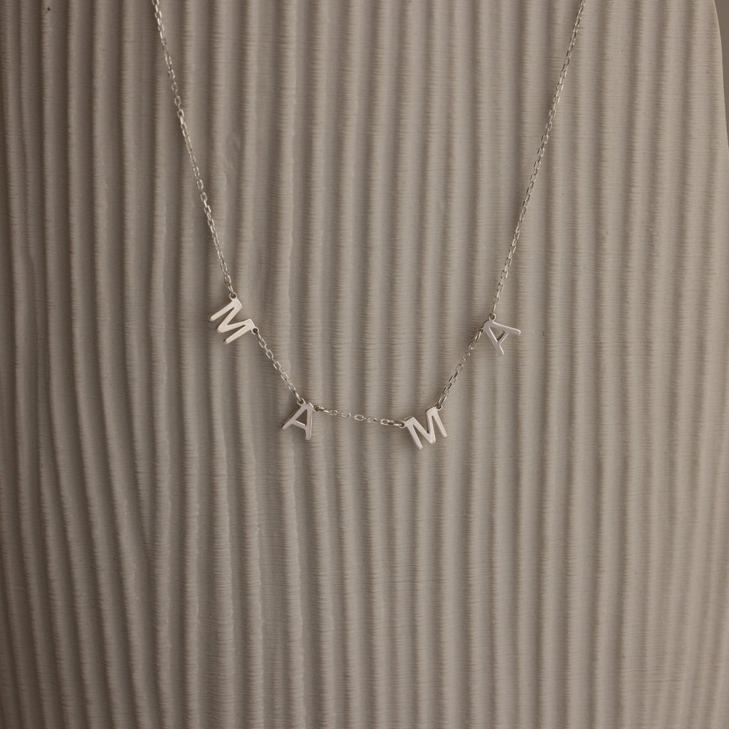 The Alice Letter Name Necklace in Sterling Silver with MAMA charms is displayed on a textured beige background—a perfect personalized necklace and thoughtful Christmas gift.