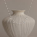 The Pave Letter Necklace in Sterling Silver, featuring charms that spell "KAYLA," is displayed against a blurred white vase, showcasing personalized elegance.