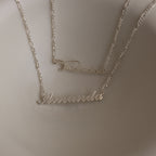 Two silver name necklace on a plain background