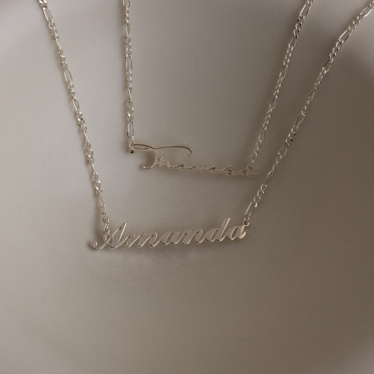 Two silver name necklace on a plain background