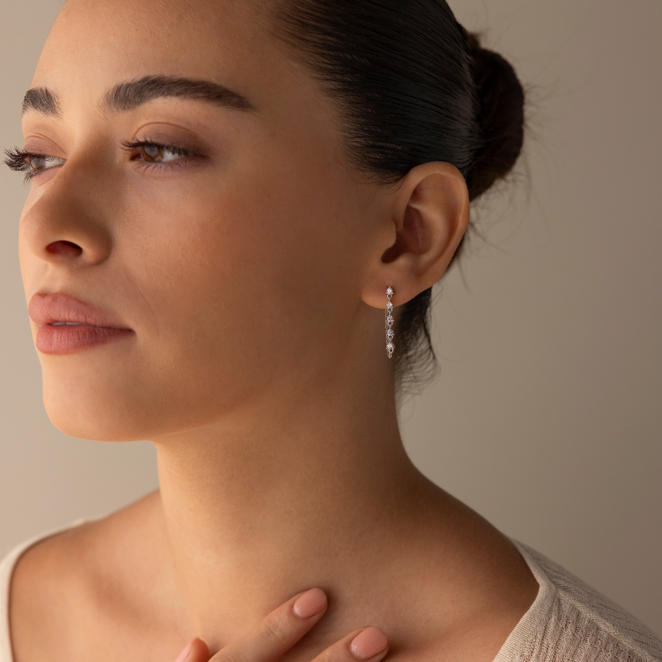 Woman with dark hair in a bun wearing Diamond Chain Drop Earrings in Silver, gazing to the left with a calm expression.