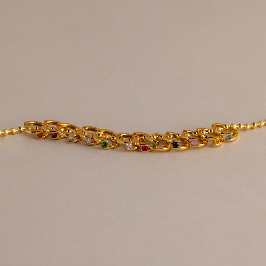 Floating Birthstone Huggies look stunning when paired with a gold chain bracelet featuring multicolored gemstones, creating a personalized jewelry statement on a neutral background.