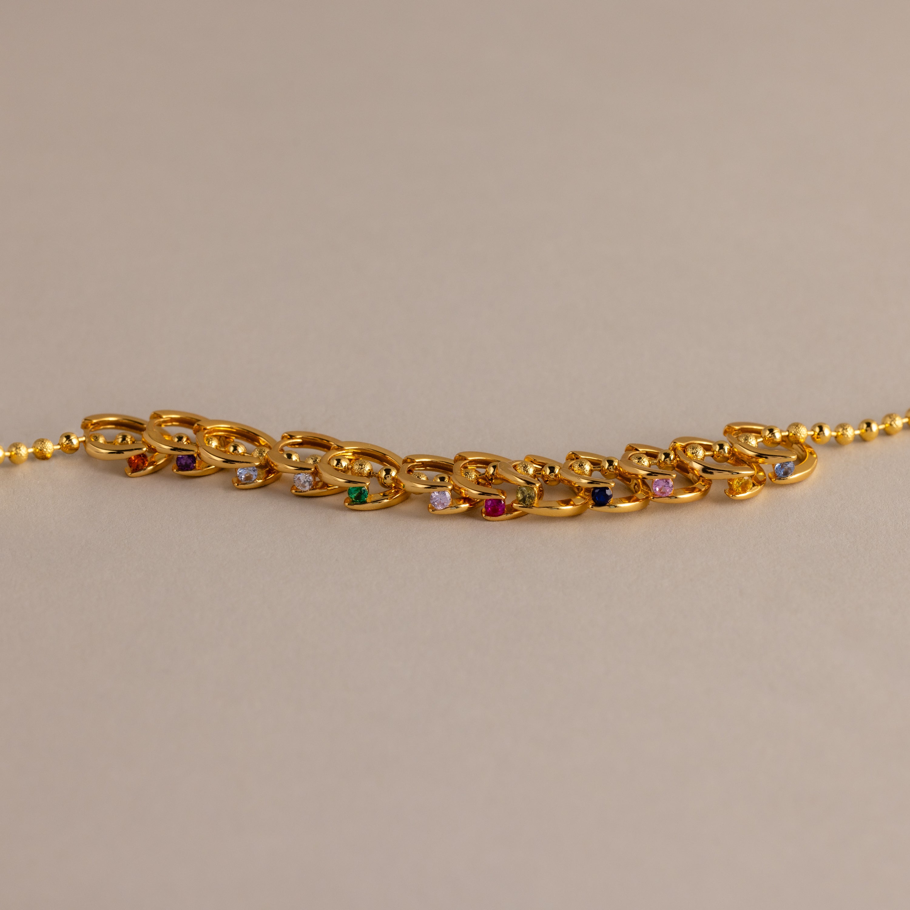 Floating Birthstone Huggies look stunning when paired with a gold chain bracelet featuring multicolored gemstones, creating a personalized jewelry statement on a neutral background.