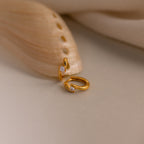 Floating Diamond Huggies showcased on a cream surface next to a beige seashell.
