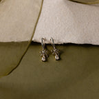Flatlay of our Teardrop Ribbon Charm Hoops in Silver against a white and green background