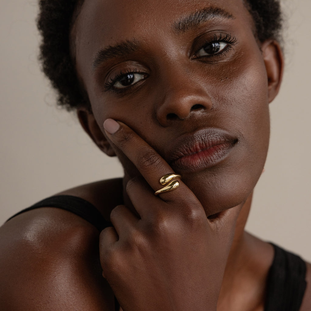 A woman with short hair wears the Duo Dome Ring, its sculptural design catching the light as she touches her face and looks at the camera.