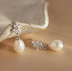 Pearl Diamond Drop Earrings in Silver with crystal accents are displayed on a beige surface next to a ceramic dish.