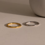 A Minimal Stacking Ring in Silver rests on a beige surface near a round white object.