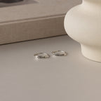 Two silver rings on a neutral surface with a beige book and vase in the background.