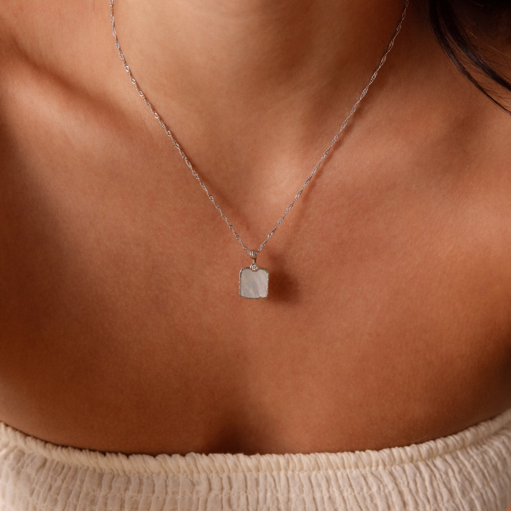 A woman layers the Square Mother of Pearl Necklace in Silver over an off-shoulder cream top.