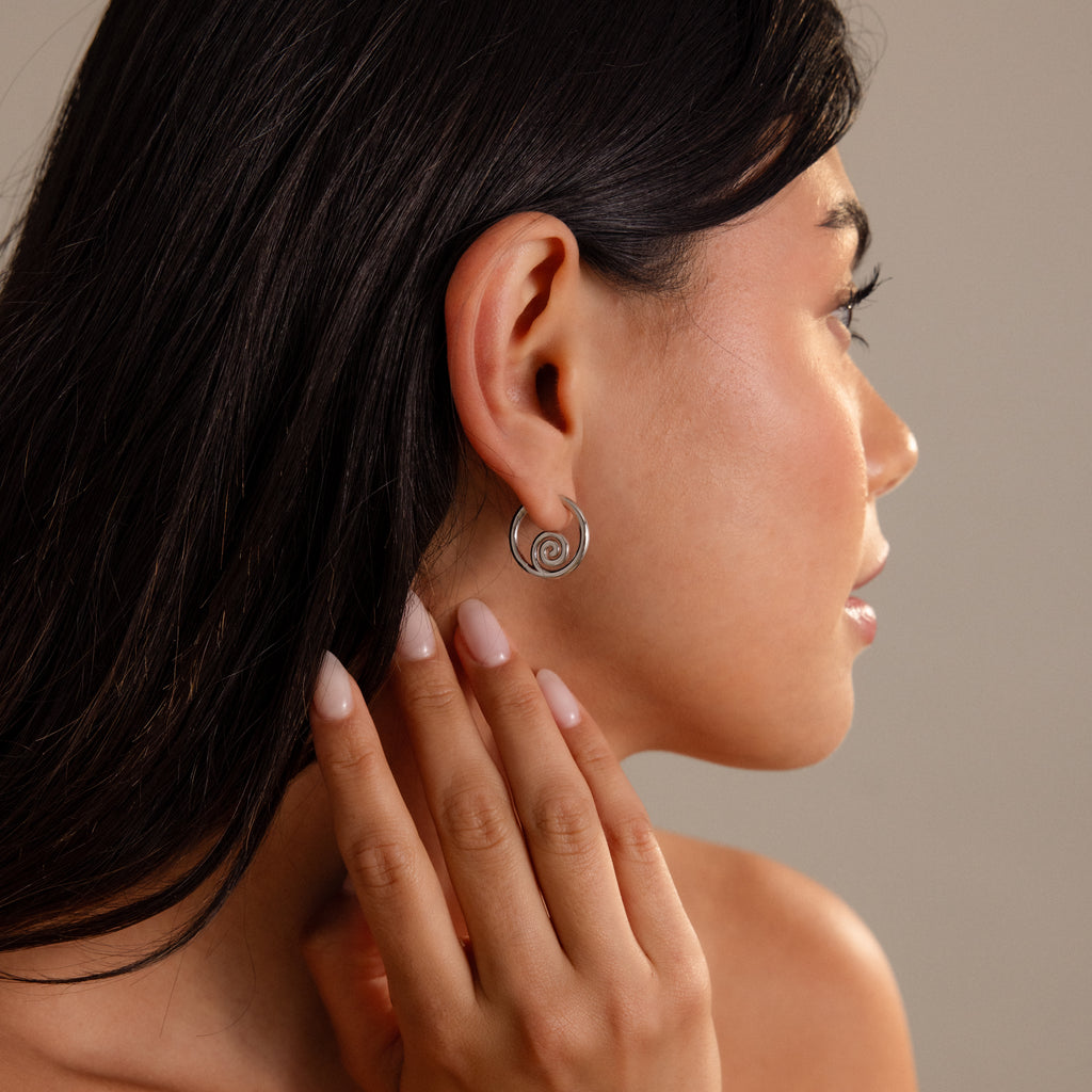 Woman with long dark hair wears Spiral Swirl Hoops in Silver, touching her neck in a side profile—perfect boho vacation jewelry.