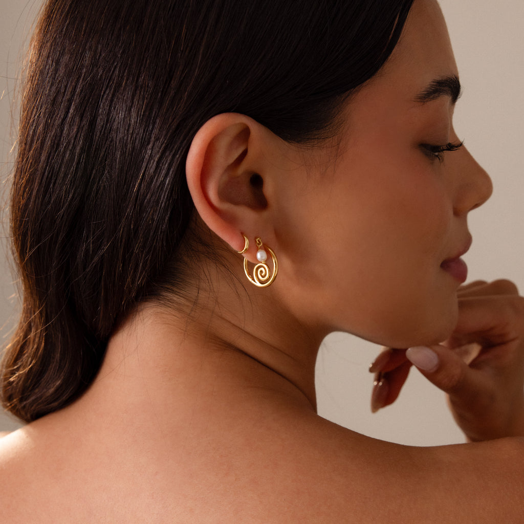 Woman with dark hair wearing Spiral Swirl Hoops in Silver, posing in profile with a soft smile—perfect boho vacation jewelry for a relaxed, beachy vibe.