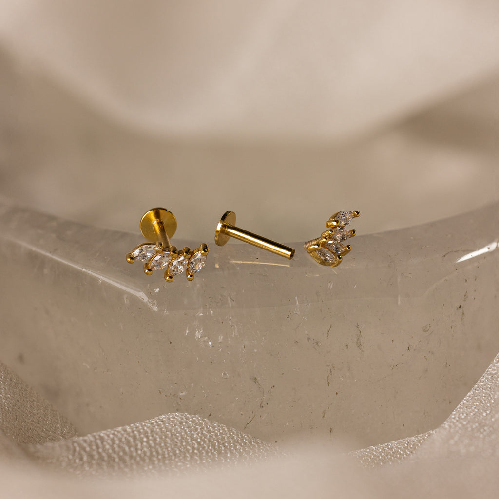 Gold stud earrings with small clear stones, shown on a crystal surface—ideal as wedding jewelry or styled with Marquise Diamond Climbers for extra elegance.
