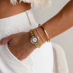 Someone in white pants wears a gold watch, the Classic Bangle, and a delicate bracelet on their wrist, highlighting chic jewelry style.