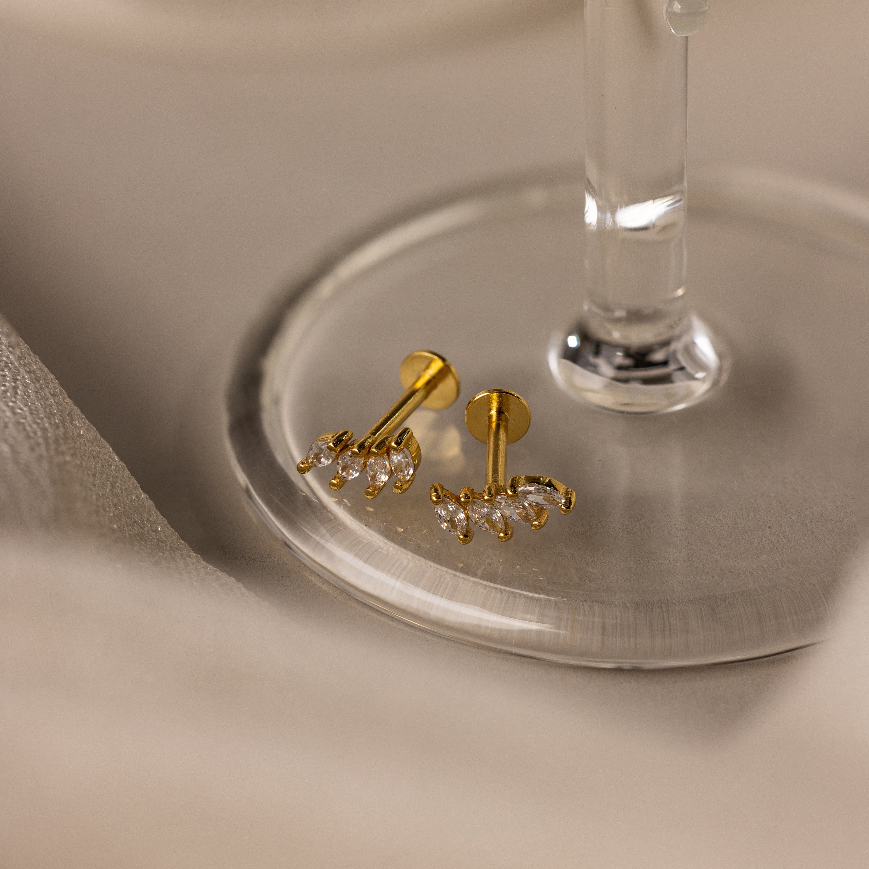 Marquise Diamond Climbers in 18K Gold, elegant earrings with sparkling diamonds, perfect as wedding jewelry, displayed on a round glass surface.