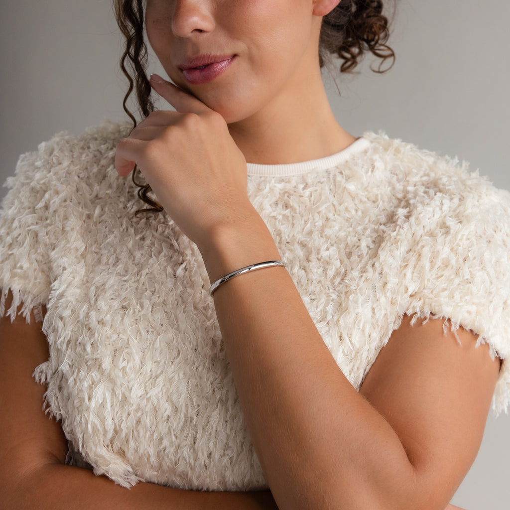 A woman in a textured white top showcases chic style, resting her chin on her hand while wearing the Classic Bangle in Sterling Silver.