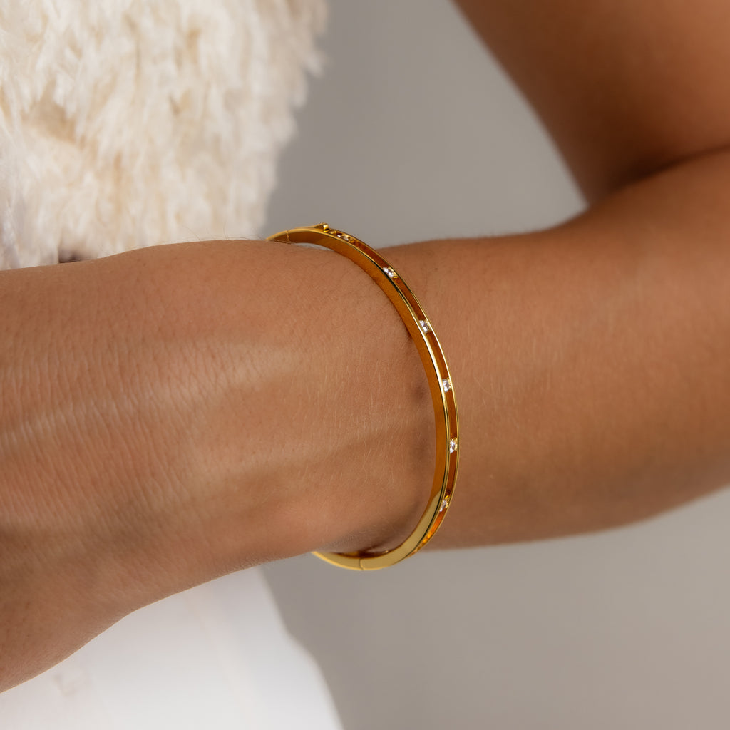 The Lace Diamond Bangle in 18K Gold, showcasing an open station design with small round diamonds, is displayed on a wrist set against a neutral background.
