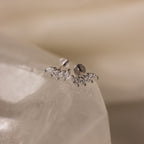 Marquise Diamond Climbers are silver stud earrings adorned with small, leaf-shaped crystals, capturing the elegance of wedding jewelry on a smooth, translucent surface.