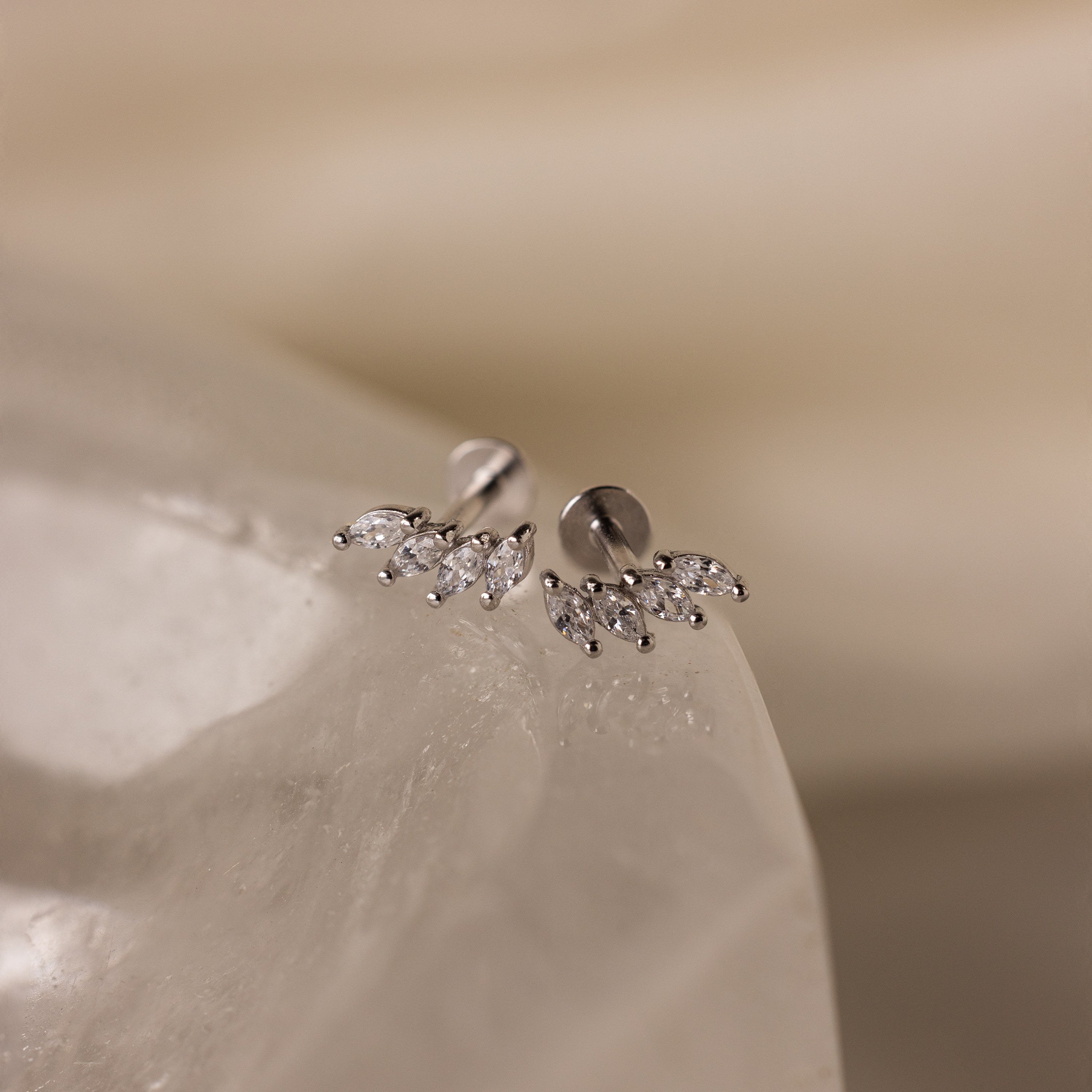 Marquise Diamond Climbers are silver stud earrings adorned with small, leaf-shaped crystals, capturing the elegance of wedding jewelry on a smooth, translucent surface.