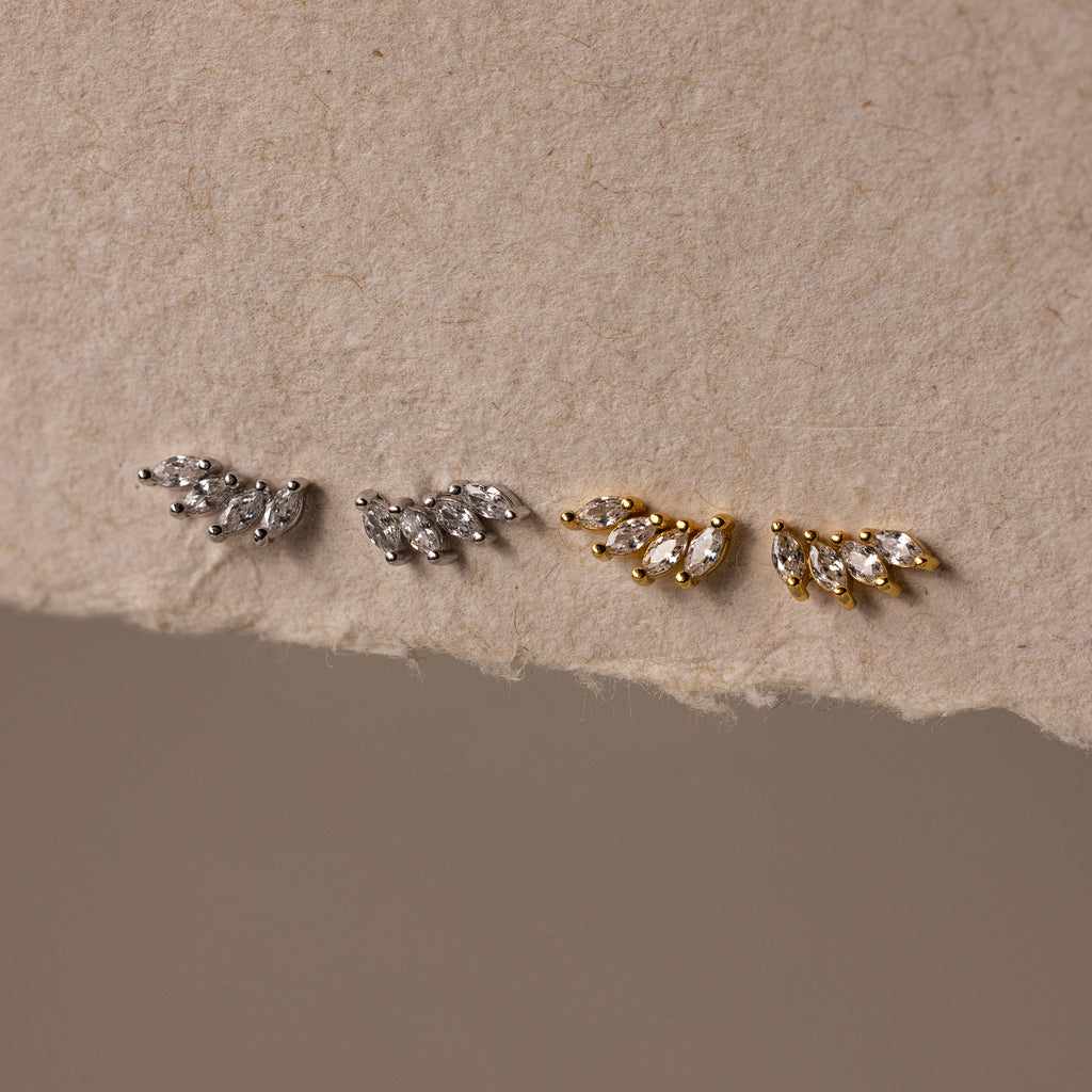 Two pairs of Marquise Diamond Climbers earrings—one silver, one gold—in a leaf-shaped design on textured beige paper; ideal wedding jewelry accents.