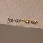 Two pairs of Marquise Diamond Climbers earrings—one silver, one gold—in a leaf-shaped design on textured beige paper; ideal wedding jewelry accents.