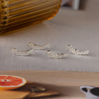 Silver name stud earrings on a neutral surface with a blurred background