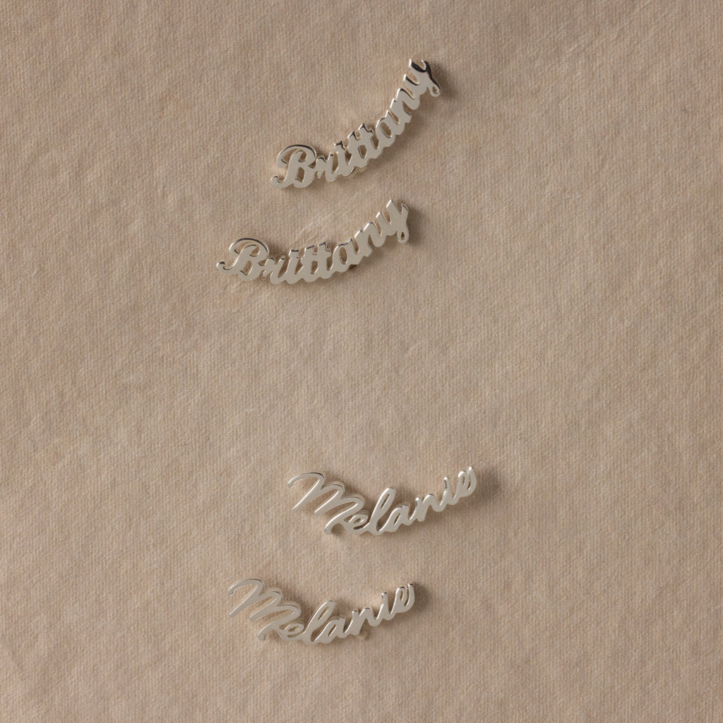 Silver nameplate earrings on a beige fabric background