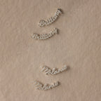 Silver nameplate earrings on a beige fabric background
