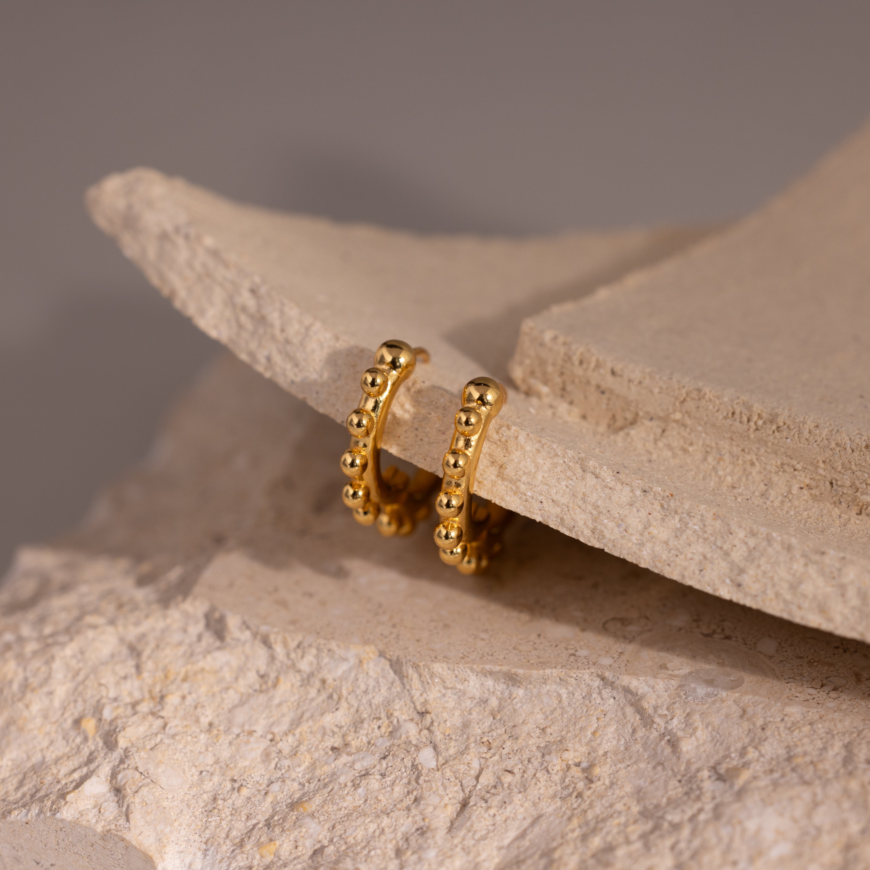 Beaded Hoops in 18K Gold featuring a beaded texture and polished beads, displayed on light beige stone.