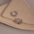 Beaded Hoops in Sterling Silver, adorned with small round accents and displayed on textured beige stone slabs, capture a subtle, textured glow.